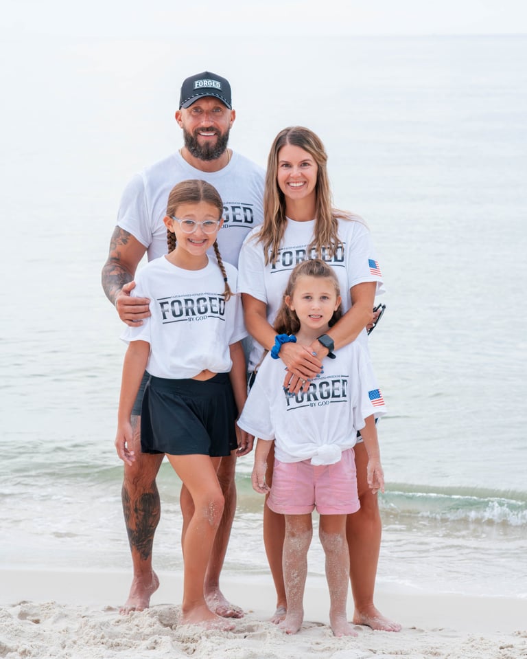 Family of four standing on beach wearing matching white Forged t-shirts, ocean and sandy shore in background